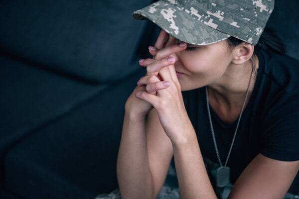 depressed woman in military uniform sitting on couch with clenched hands at home