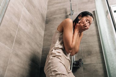 depressed woman covering face with hands while crying in shower at home clipart