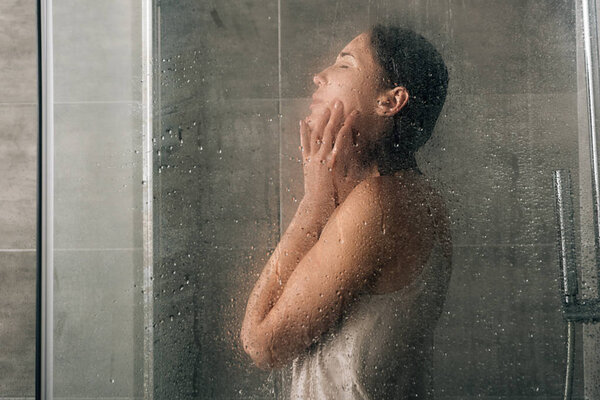 sad depressed woman in shower through glass with water drops