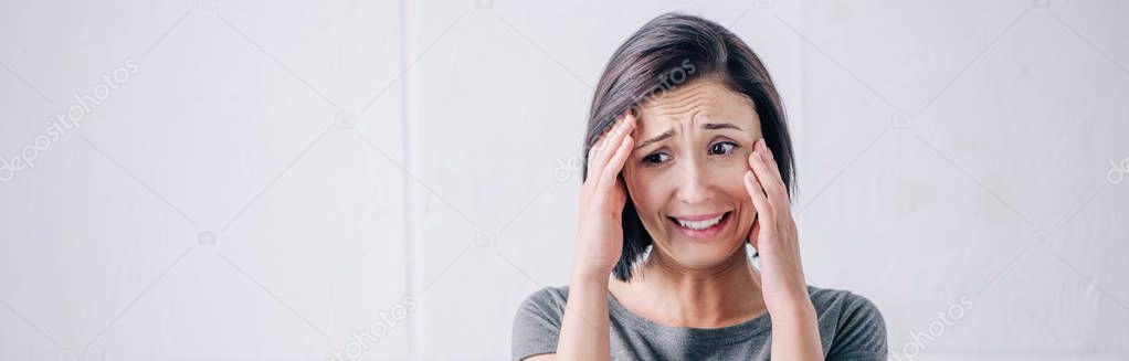 panoramic shot of depressed brunette woman touching face and crying at home