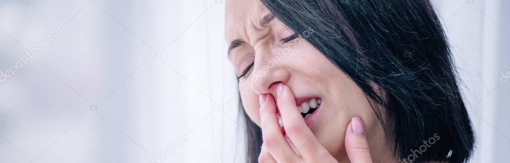 panoramic shot of depressed brunette woman crying and covering mouth at home