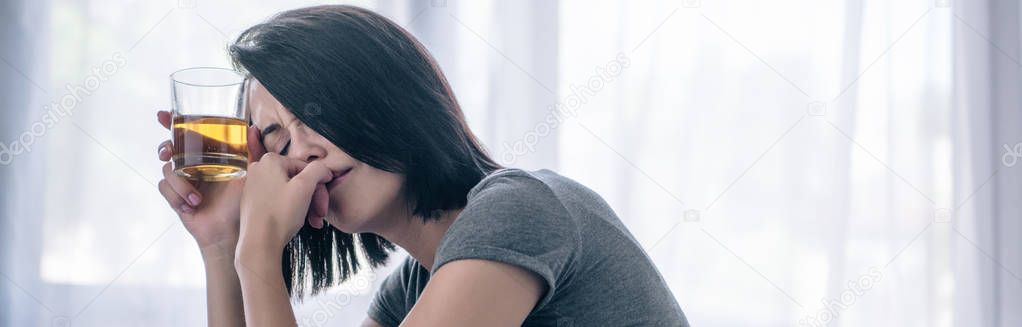 panoramic shot of depressed woman with whiskey glass at home