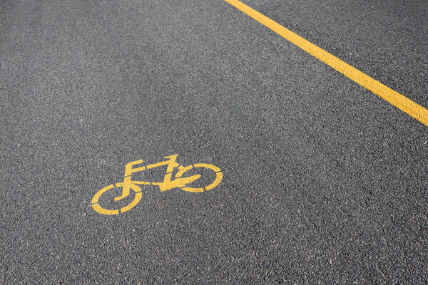 желтый символ велосипедной дорожки на сером асфальте
 
