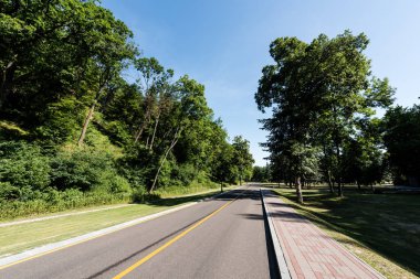 road with yellow line near walkway and park with green trees clipart