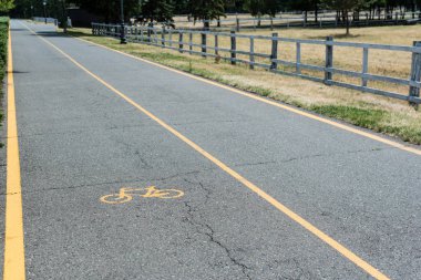 yellow symbol of bicycle lane on grey asphalt near fence  clipart