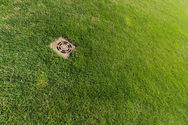 metallic manhole cover on green fresh grass 