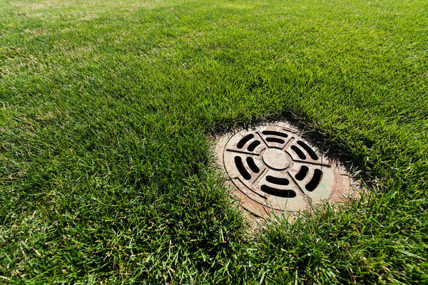 metallic manhole cover on green and fresh grass 