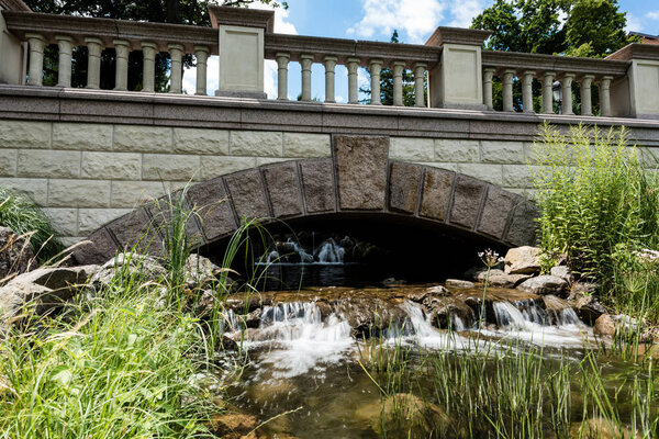 stone bridge near steam with flowing water on rocks in park 