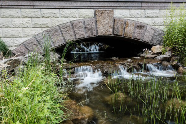 stone bridge near steam with water flowing on rocks in park 