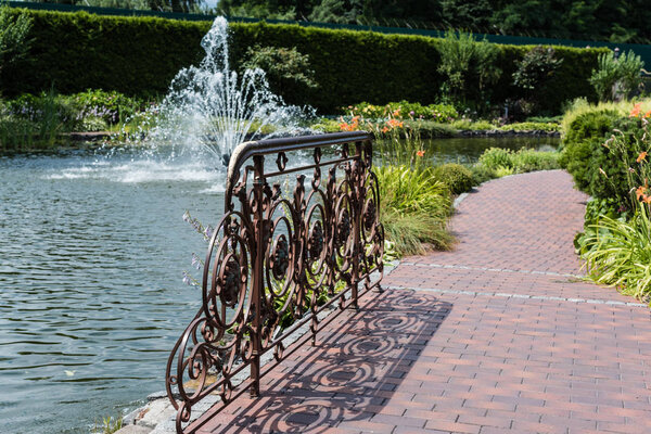 selective focus of metallic fence on bridge near lake with fountain 