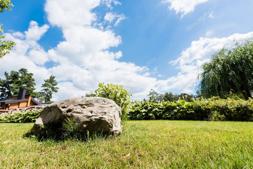 selective focus of rock on green grass against blue sky with clouds 