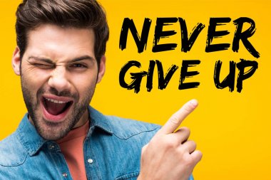 handsome man pointing with finger at never give up lettering and winking isolated on yellow clipart