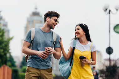 yakışıklı adam ve asyalı kadın gülümseyerek ve kağıt bardak tutarak 