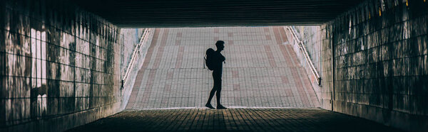 panoramic shot of young adult man with backpack in tunnel 