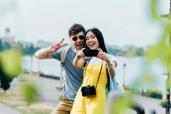Przystojny Człowiek Pokazując Znak Pokoju Asian Kobieta Biorąc Selfie — Zdjęcie stockowe