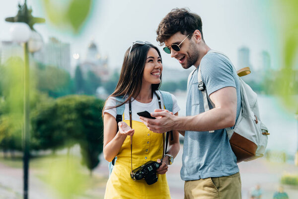 handsome man holding smartphone and asian woman talking with him 