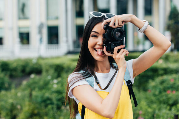 attractive and asian woman with glasses sticking out tongue and taking photo  