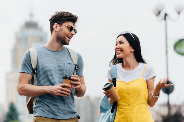 handsome man and asian woman smiling and holding paper cups 
