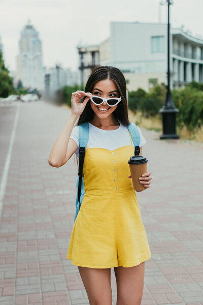  asian woman holding paper cup with coffee and looking away 