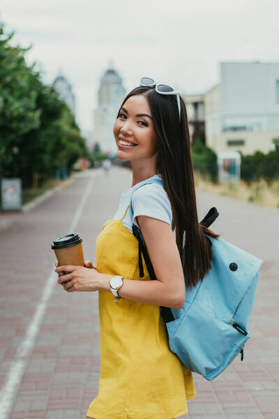  asian woman holding paper cup with coffee and looking at camera 