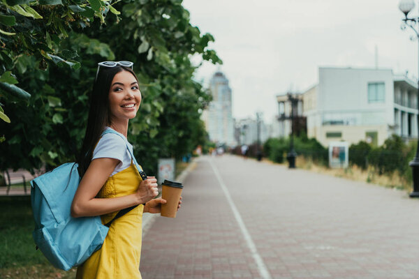  asian woman holding paper cup with coffee and looking away 
