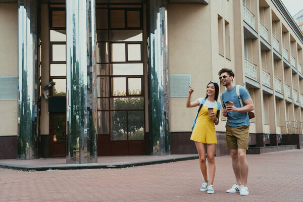 handsome man holding paper cup and asian woman pointing with finger 