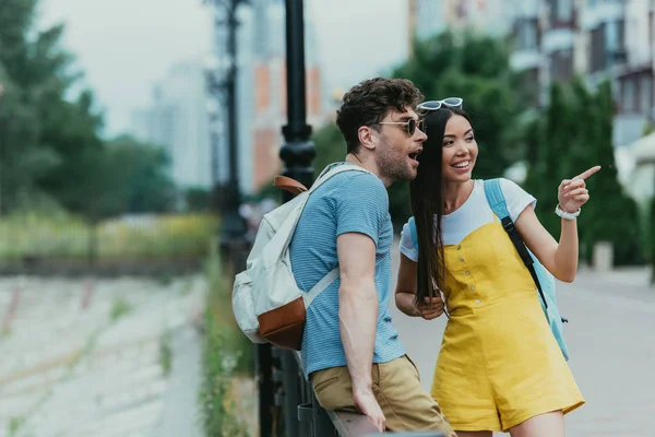 yakışıklı adam uzağa bakıyor ve asyalı kadın parmakla işaret 