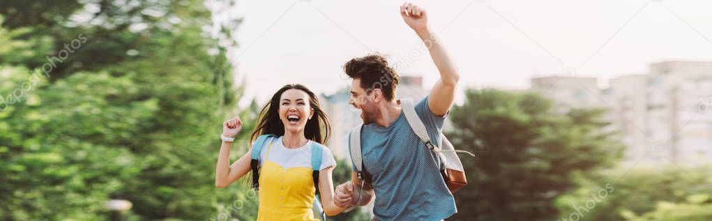 panoramic shot of handsome man and asian woman running and showing yes gesture 