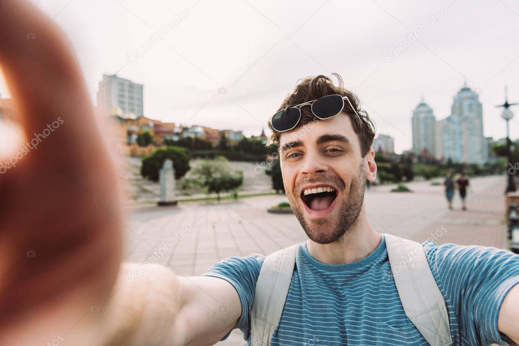 selective focus of handsome man with glasses smiling and taking selfie 