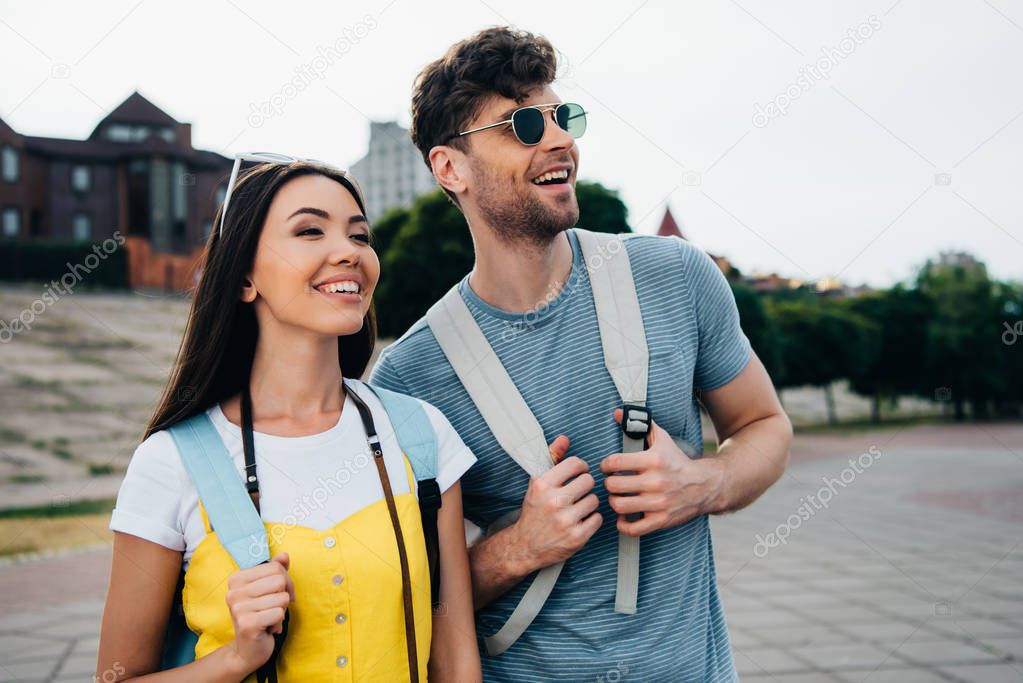 handsome man and asian woman with backpacks looking away 