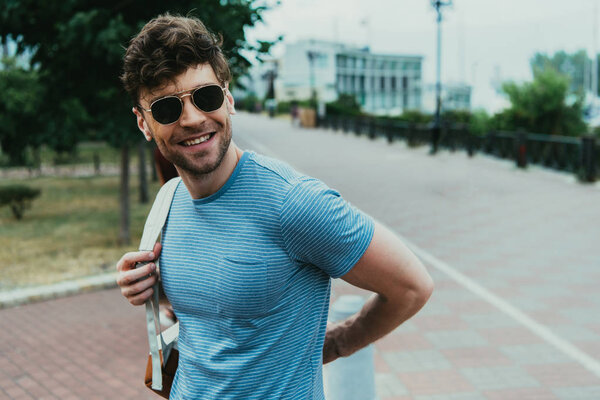 smiling and handsome man in t-shirt with backpack and glasses 