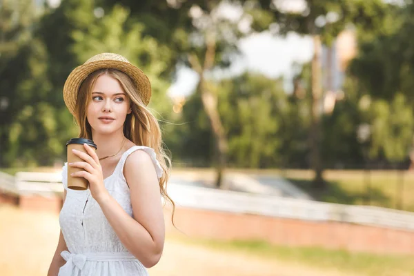 美丽的女孩在白色礼服和草帽拿着纸咖啡杯 看着远 — 图库照片