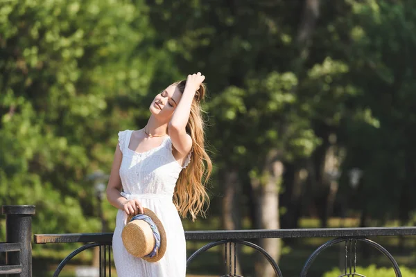 Hermosa Chica Vestido Blanco Sosteniendo Sombrero Paja Mientras Está Pie — Foto de Stock