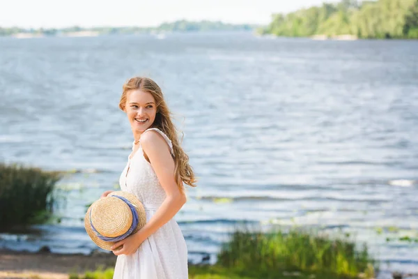 Genç Kız Saman Şapka Tutarak Uzağa Bakarken Nehir Kıyısında Duran — Stok fotoğraf