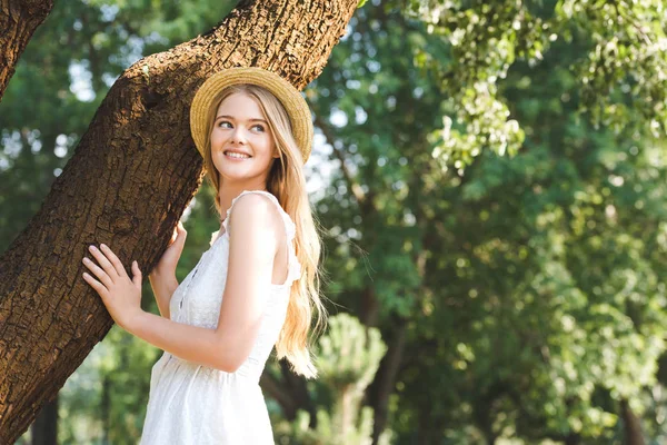 Beyaz Elbise Hasır Şapka Ağacın Gövdesi Yakınında Duran Güzel Genç — Stok fotoğraf