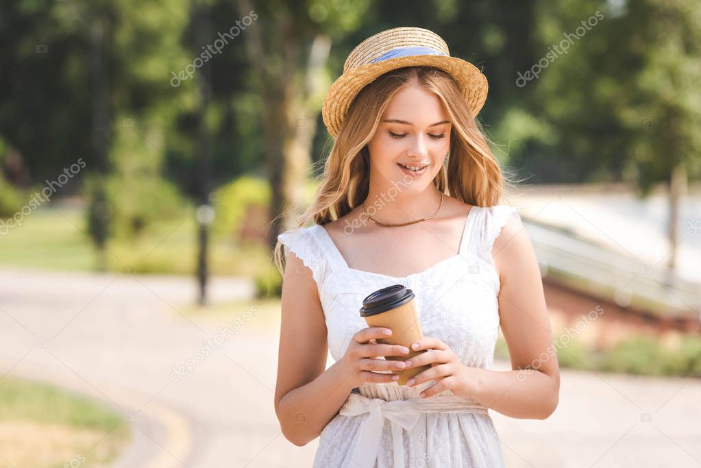 beautiful girl in white dress and straw hat holding paper coffee cup and walking with closed eyes