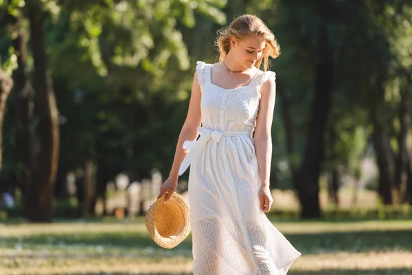 Hermosa Chica Vestido Blanco Sosteniendo Sombrero Paja Mientras Sonríe Pie — Foto de Stock