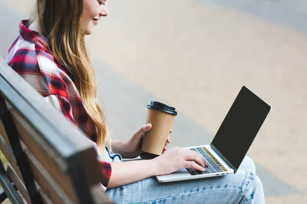 公園の木製のベンチに座ってノートパソコンを使用しながら 紙のコーヒーカップを保持するカジュアルな服の美しい女の子の選択的な焦点 — ストック写真