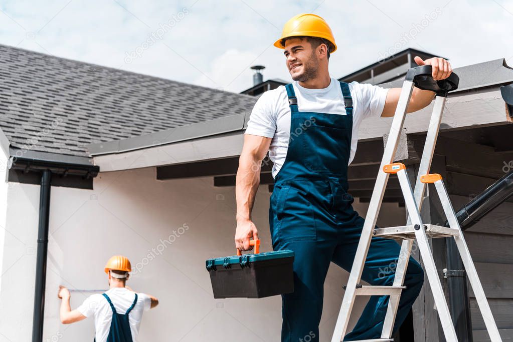 selective focus of happy workman standing on ladder with toolbox near coworker 