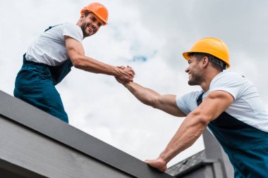 low angle view of cheerful handymen in helmets holding hands  clipart