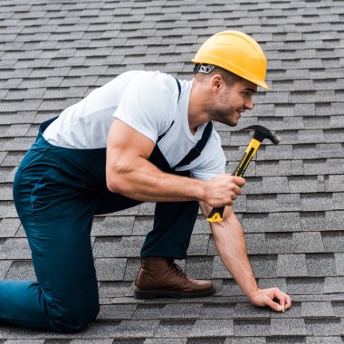 repairman in helmet holding hammer while repairing roof in house  clipart