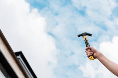 cropped view of handyman holding hammer against blue sky  clipart