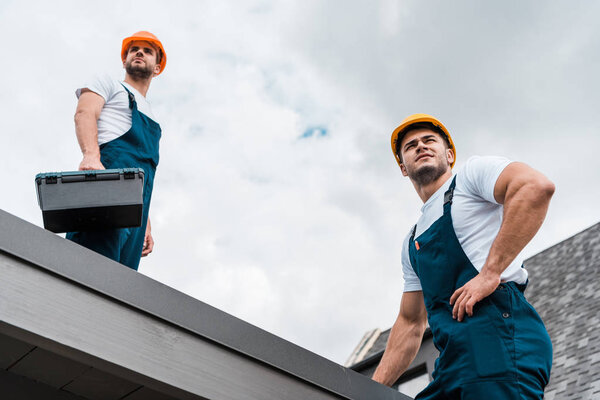 low angle view of handsome handymen in helmets against sky with clouds 