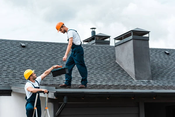 Handwerker Helm Übergibt Werkzeugkiste Hübschen Kollegen Der Auf Dach Steht — Stockfoto