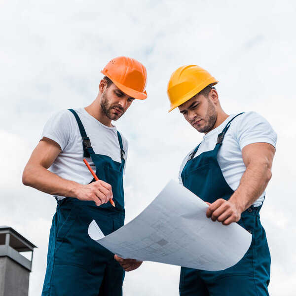 low angle view of handsome builders in uniform looking at paper with plan 