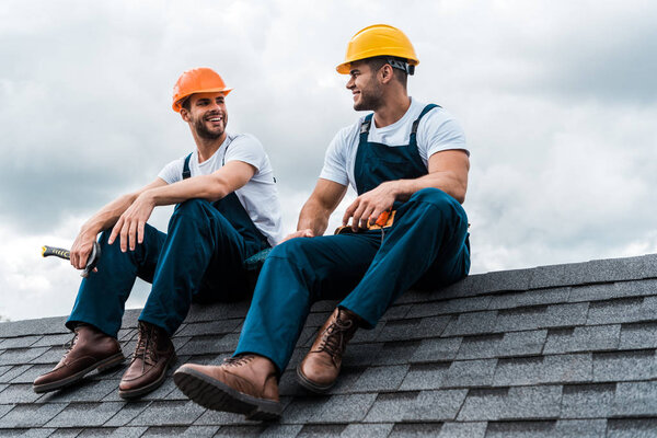 happy handymen in helmets and uniform sitting on rooftop 