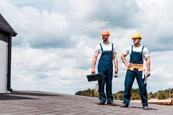 handsome handymen standing with toolbox near coworker holding digital tablet 