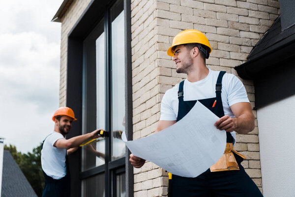 selective focus of happy architect holding blueprint near coworker 