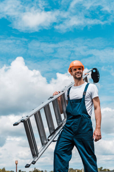 happy repairman holding ladder and smiling against blue sky with clouds 