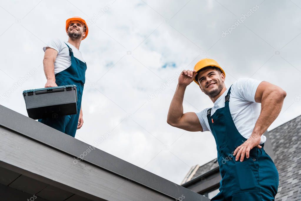 low angle view of happy handymen in helmets against sky with clouds 